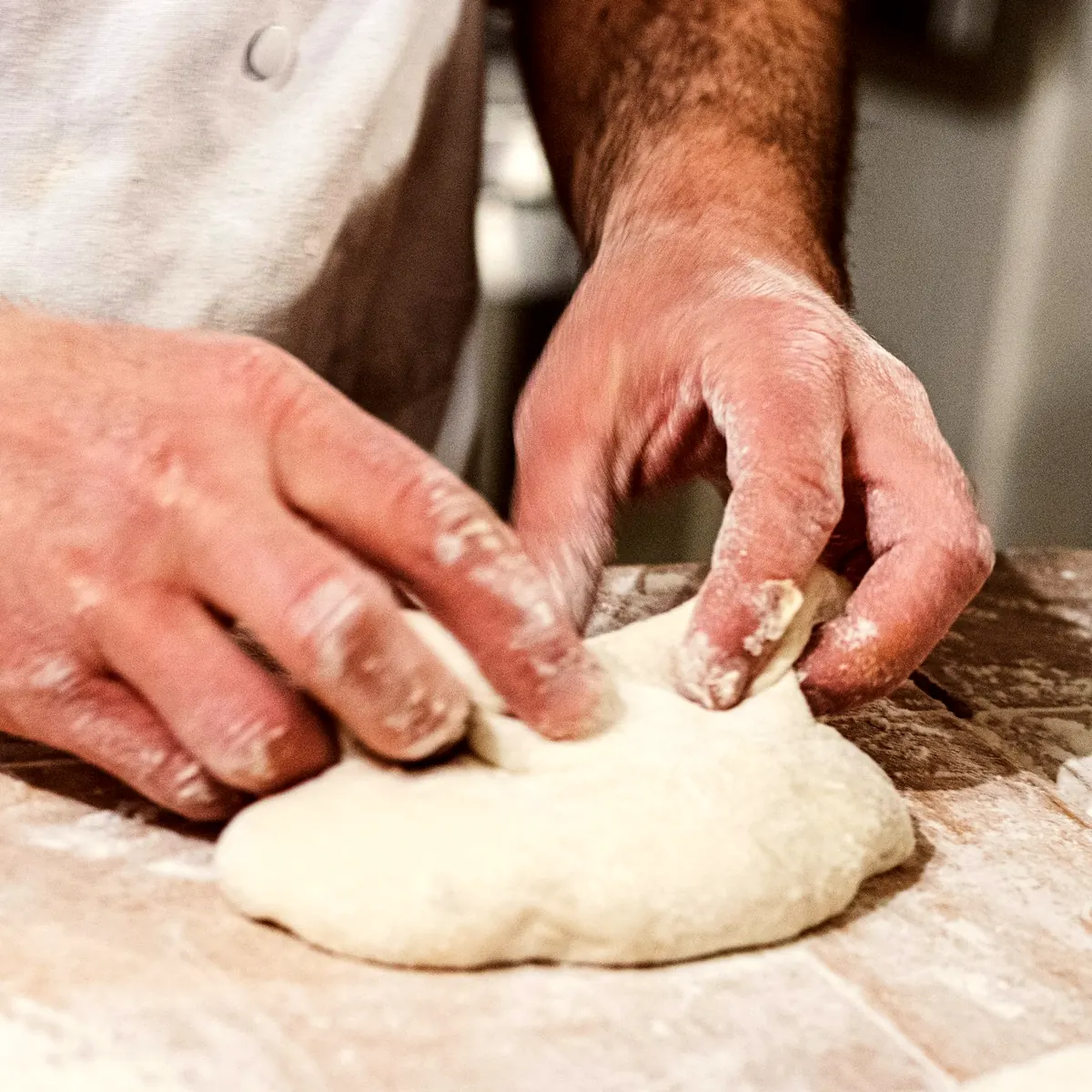 Mains qui façonnent la pâte sur le plan de travail fariné